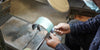 Craftsman carefully grinding and shaping a steel razor blade in a workshop, showcasing the craftsmanship behind modern straight razor designs.