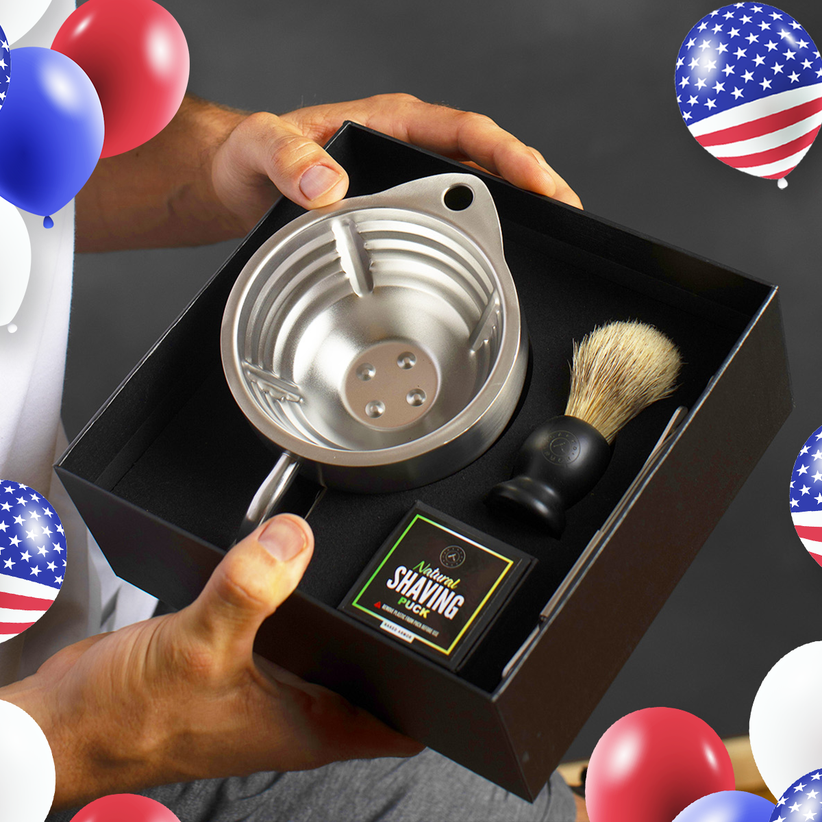 A man holding open a black premium Naked Armor gift box containing the Silver Fox Scuttle kit, complete with a stainless steel scuttle, synthetic shaving brush, and a natural shaving soap puck.
