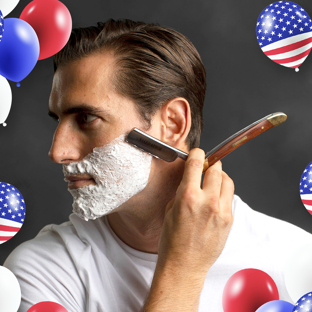 Profile view of a man using the Naked Armor Solomon Straight Razor to shave his face with lather, framed by red, white, and blue balloons.